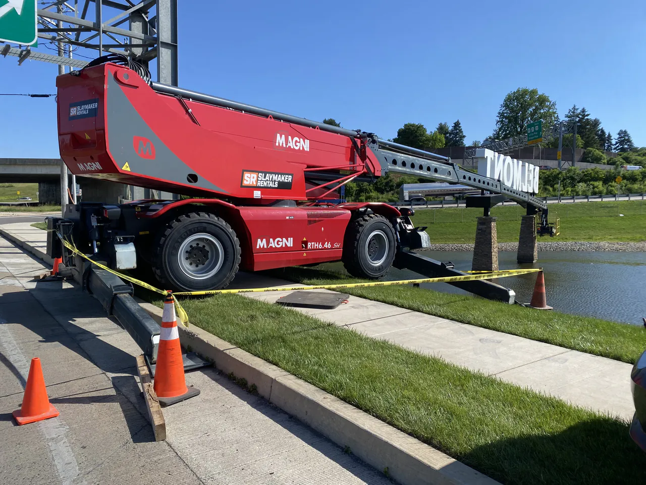 A Slaymaker Rentals Magni rotating telehandler reaching across a pond to the Belmont sign